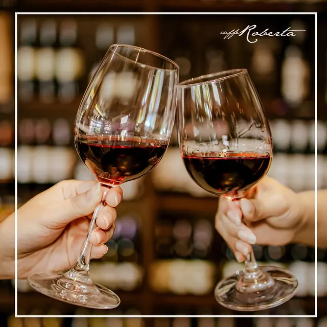 Brindisi con due calici di vino rosso davanti alla vetrina delle bottiglie